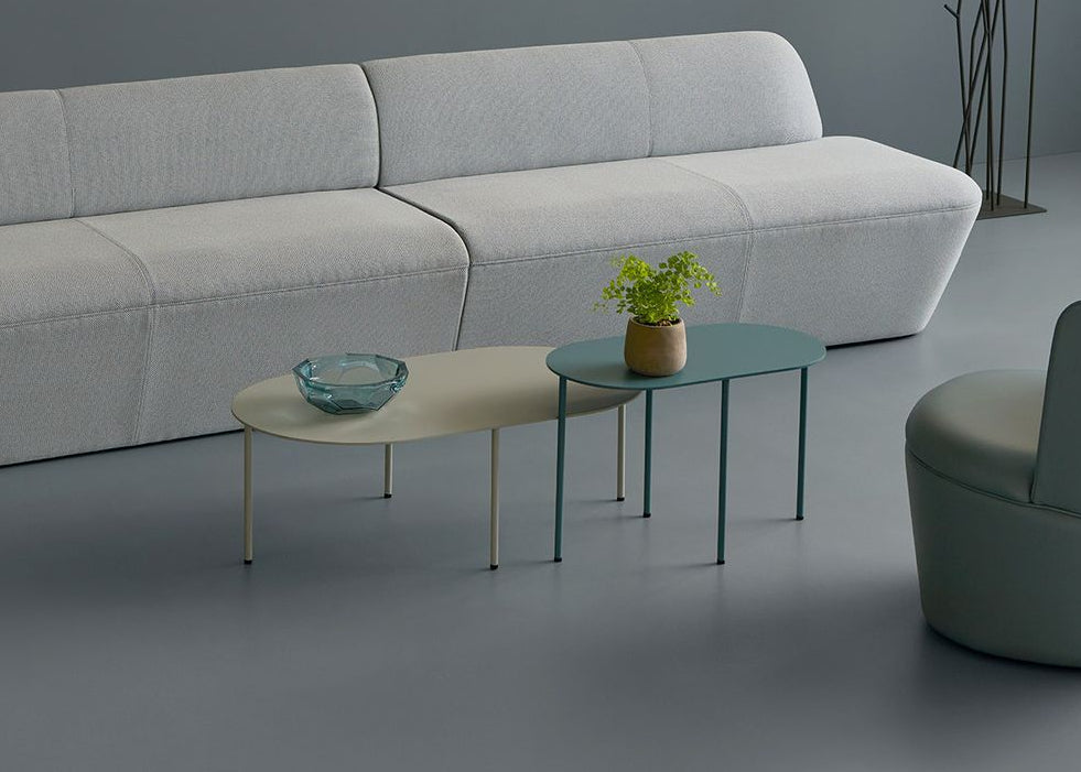 Modern living room setup with a light gray sofa, armchair, and coffee tables on a gray floor.